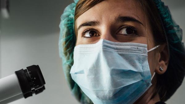 Woman Wearing Scrubs Using Microscope